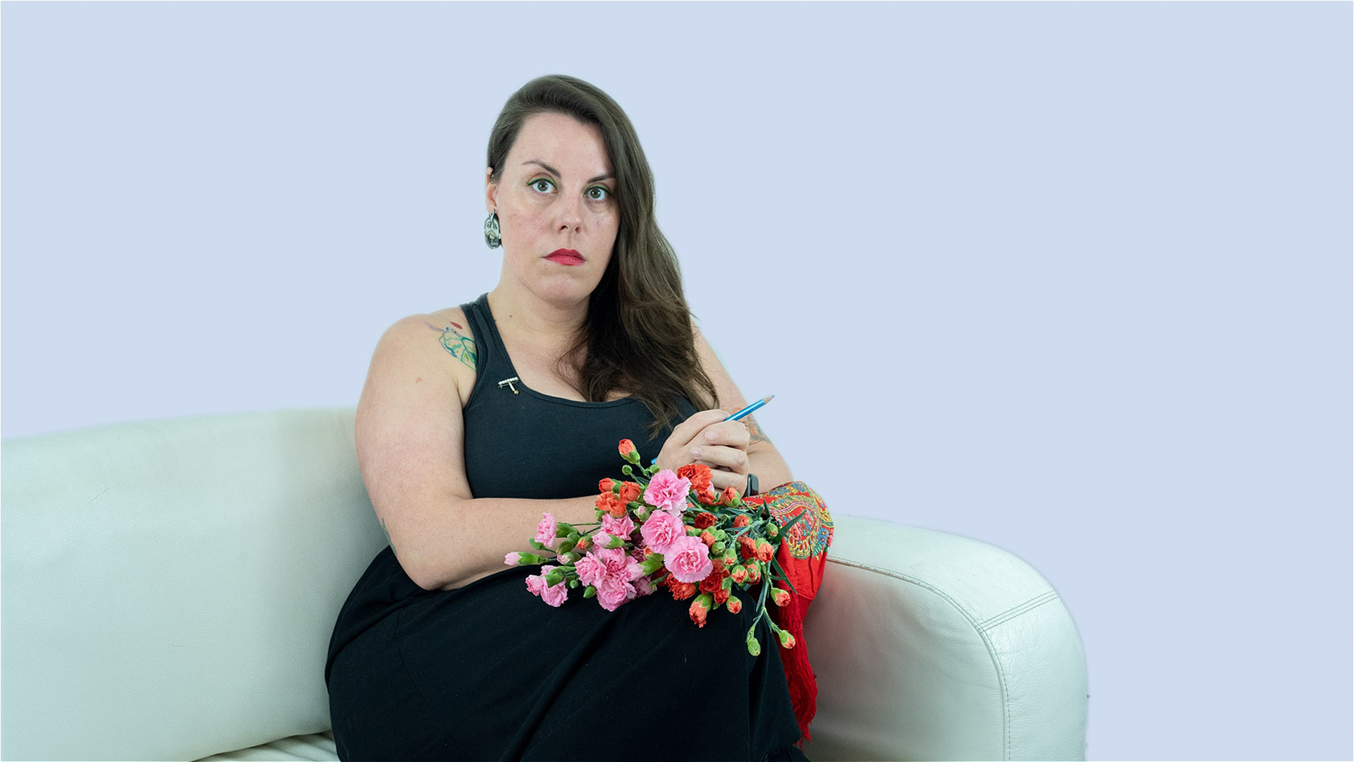 Mariana holding a bouquet of pink and red carnations, held together by a Viana do Castelo traditional scarf and a blue pencil. Mariana is wearing black clothes, a cross brooch, and an earring representing António Variações. They are wearing green eye shadow and red lipstick.