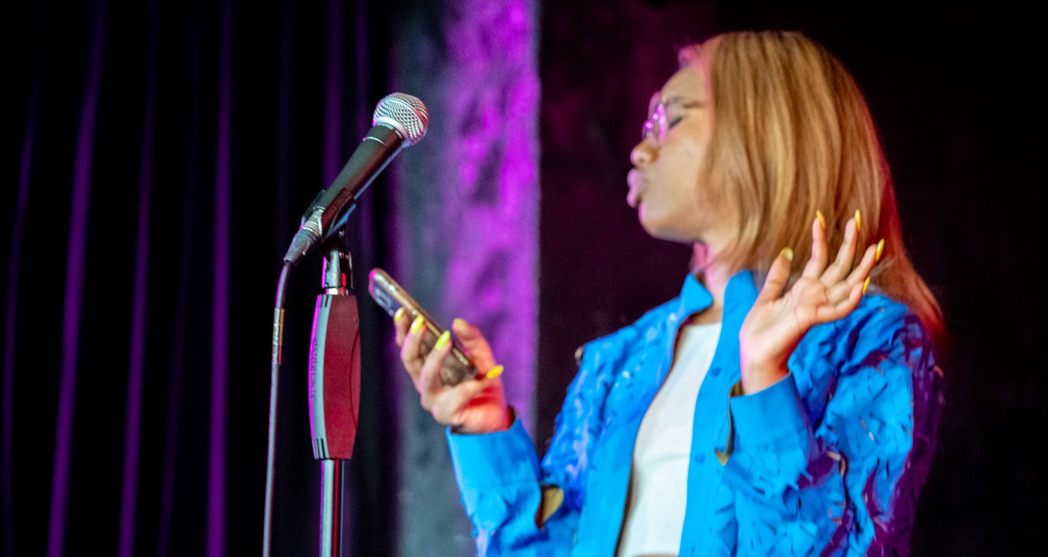 Kemah, holding a microphone, wearing a blue blazer